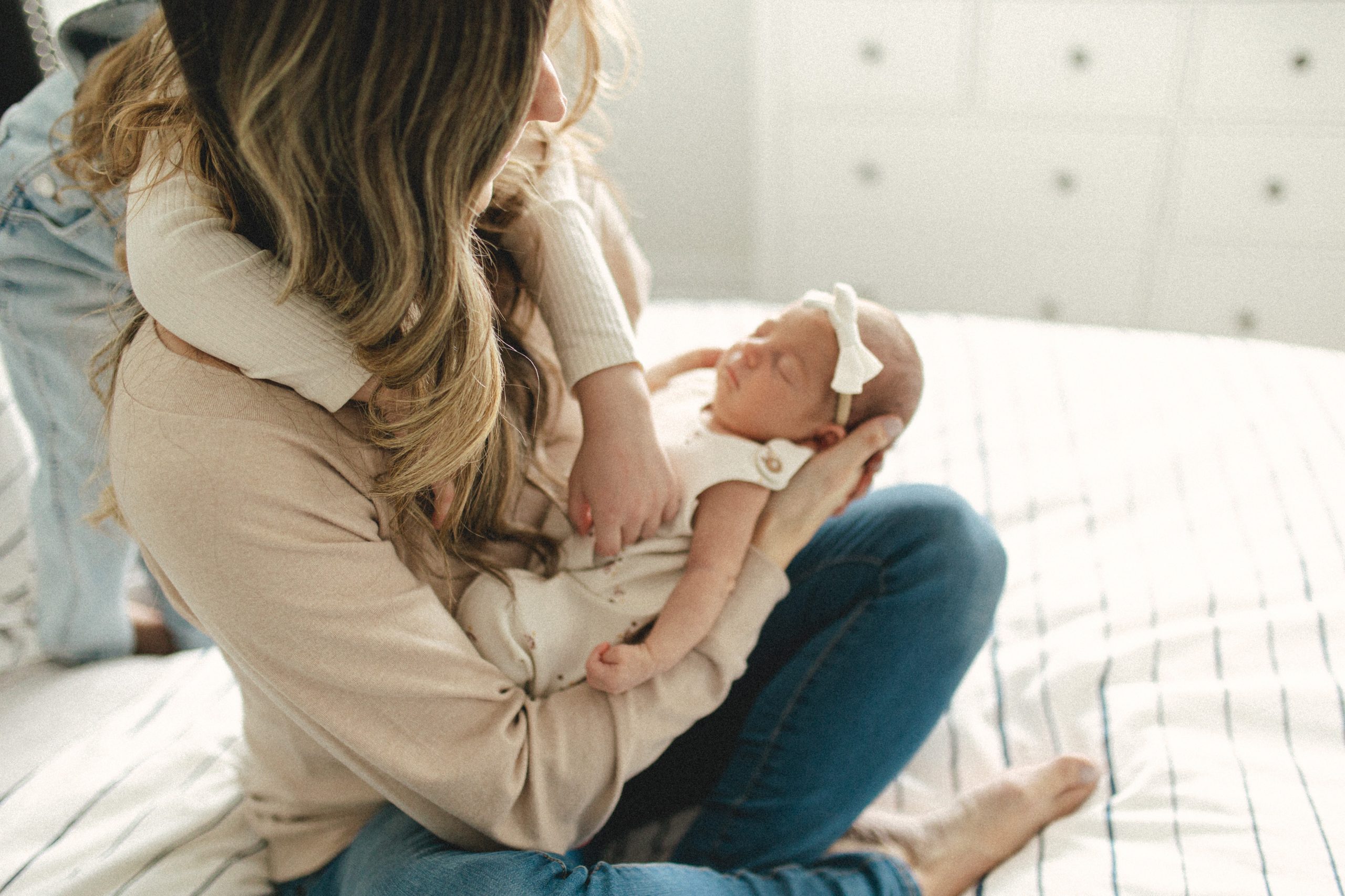 Mother holding daughter and newborn baby on bed